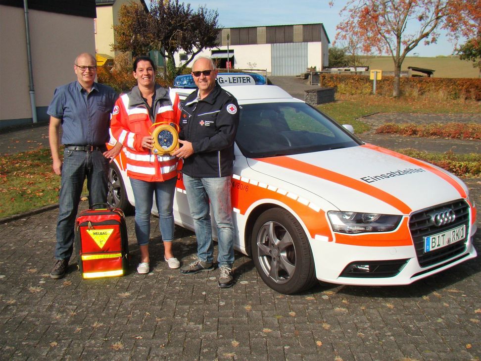 DRK Leiter Oswald Benzel und der Rommersheimer Ortsbürgermeister Helmut Nober übergeben First-Responderin Tatjana Weiers die neue Notfalltasche mit Defibrillator. Foto: FF