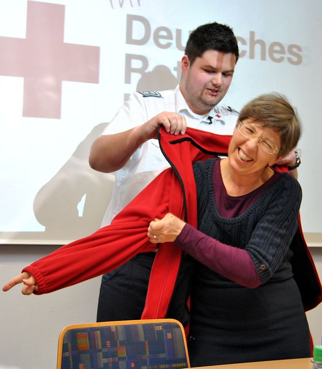 Das Outfit muss stimmen: Gemeinschaftsleiter Daniel Pöthmann hilft Angelika Gräber-Stupp, der neuen Vorsitzenden des DRK-Ortsvereins Euskirchen, in die rote Jacke. Foto: Renate Hotse/pp/Agentur ProfiPress