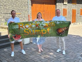 Der Platz an der Thürer Dorfscheune wird am 22. August zum „Rock am Sumpf“-Ground. Ortsbürgermeister Lukas Ellerich (links), Laura Berresheim und Jörg Lempertz, Schirmherr und Bürgermeister VG Mendig, rühren schon einmal die Werbetrommel.