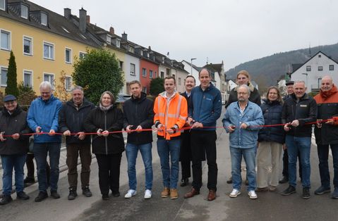 Baudezernent Thilo Becker und Ortsvorsteher Hans-Alwin Schmitz (vorne, 5. und 4. v. r.) sowie Vertreterinnen und Vertreter der beteiligten Firmen und Ämter, des Stadtrats und des Landesbetriebs Mobilität durchschneiden ein Band zur Verkehrsfreigabe der Eisenbahnstraße.