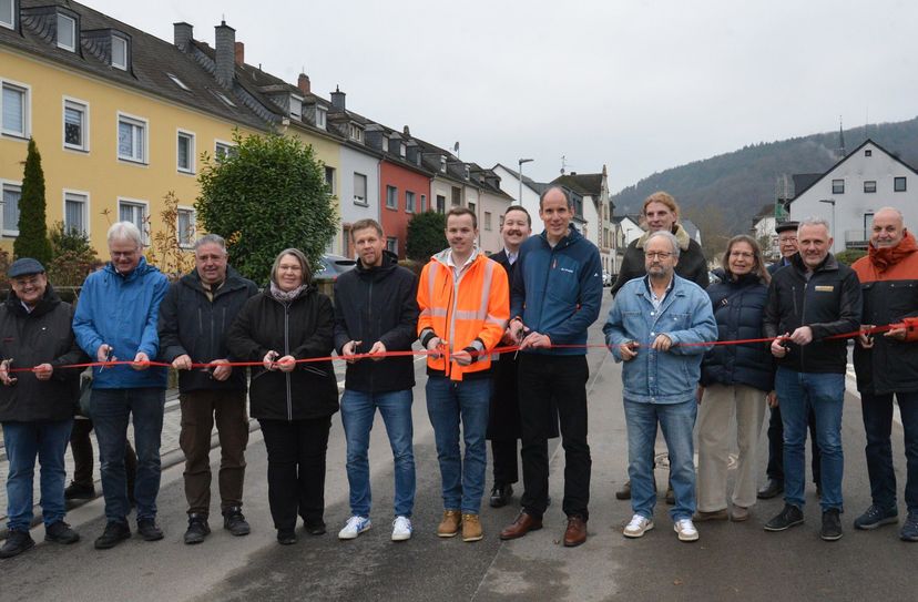 Baudezernent Thilo Becker und Ortsvorsteher Hans-Alwin Schmitz (vorne, 5. und 4. v. r.) sowie Vertreterinnen und Vertreter der beteiligten Firmen und Ämter, des Stadtrats und des Landesbetriebs Mobilität durchschneiden ein Band zur Verkehrsfreigabe der Eisenbahnstraße.