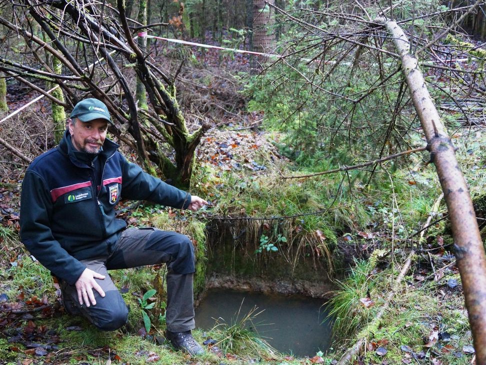 Förster Jens Willen zeigt an einem Bodeneinschlag, dass sich durch die tonreiche Erdschicht das künstlich angelegte Erdloch mit Wasser füllt. Die Fichten auf dieser Fläche wurzeln nicht tiefer als 20 Zentimeter. Foto: Dietmar Ebi