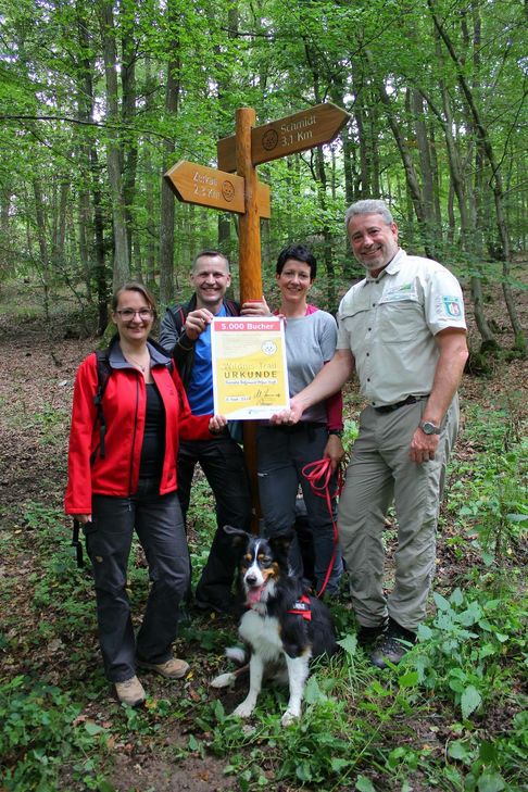 Sie sind die 5000. Bucher des Arrangements: Zusammen mit Hund Quincy durchqueren Renate Hoffmann und Stefan Vogt (Bildmitte) den gesamten Nationalpark Eifel auf dem Wildnis-Trail. Michael Lammertz (r.), Initiator des Wildnis-Trails, und Cornelia Freuen (l.) von der Buchungsstelle des Wildnis-Trails überreichten dem Paar eine besondere Urkunde und Gutscheine für die Erlebnisausstellung »Wildnis(t)räume« im Nationalpark-Zentrum Eifel.