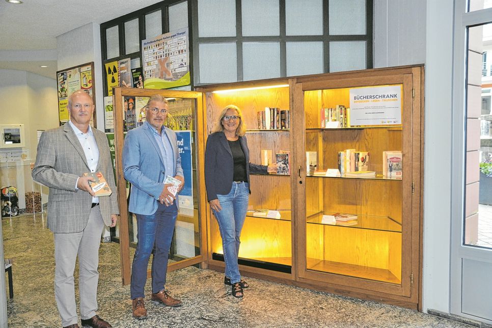 Bürgermeister Bernd Goffart mit Angelika und Herbert Stollenwerk vor dem neuen Bücherschrank im Simmerather Rathaus.