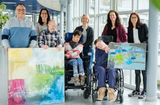 Gemeinsam präsentieren der Betriebsratsvorsitzende Sascha Murphy (links), Yvonne Pick-Becker (rechts), Assistenz des Betriebsrates, Mitarbeitende der Lebenshilfe Rhein-Hunsrück sowie die Kunstschaffenden ihre ausdrucksstarken Gemälde – ein sichtbares Zeichen gelebter Inklusion.