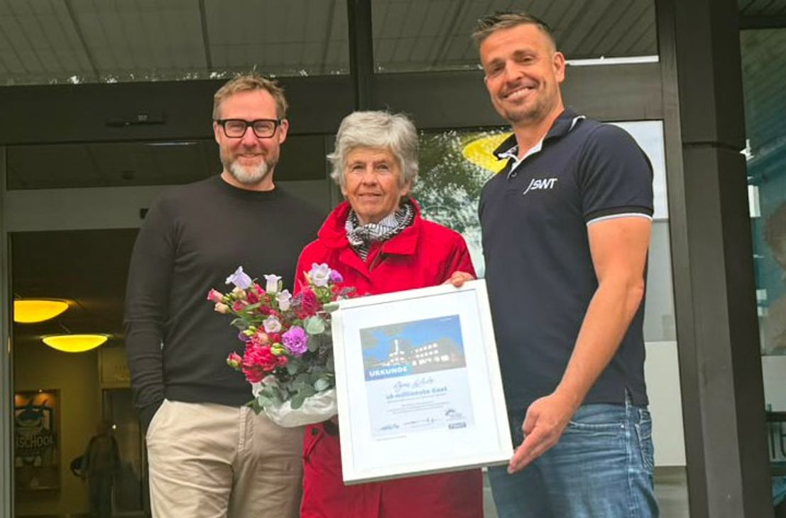 Dirk Eis (SWT-Prokurist), Agnes Wirtz und Thomas Bohn (SWT) überreichen Blumenstrauß und Urkunde.