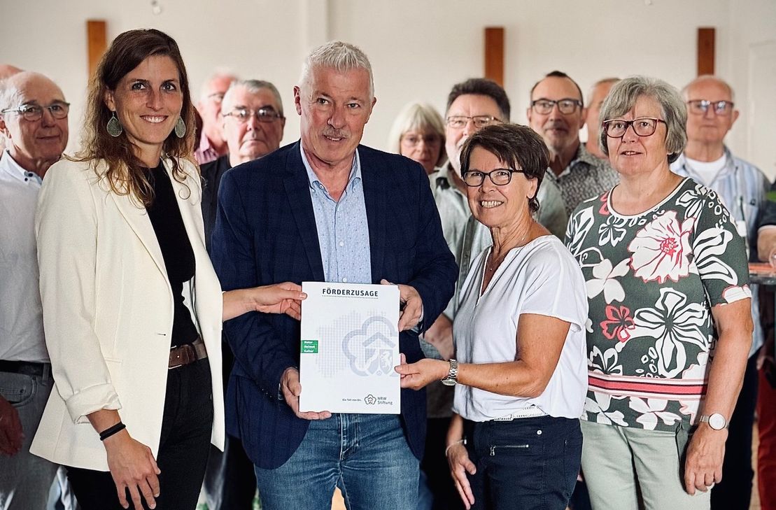 Prof. Dr. Karl-Heinz Erdmann, Vorstandsmitglied der NRW-Stiftung (2.v.l.), überreicht an die Vorsitzende des Eifelvereins Monschau-Höfen, Monika Jakobs (3.vl.), im Beisein zahlreicher Vereinsmitglieder und der Bürgermeisterin von Monschau, Dr. Carmen Krämer (l.), die Förderurkunde über 35.000 Euro für die Erneuerung von Haus Seebend und des Webereimuseums.