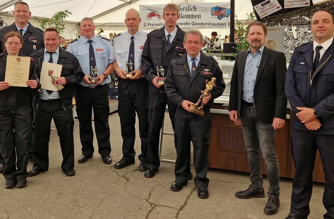 Sonja Dieler-Weber, Stephan Hammes, Daniel Walter, stellv. Wehrführer Jens Adams, Wehrführer Reinhold Pies, Thorsten Louis, Bernhard Hommer, Bürgermeister Peter Unkel und Wehrleiter Andre Stein im Festzelt der Gondershausener Kirmes neben der Baustelle für das neue Feuerwehrhausen.