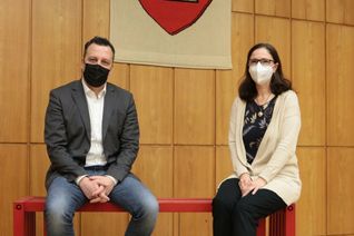 Bürgermeister Sacha Reichelt und Gleichstellungsbeauftragte Barbara Brieden sitzen auf der roten Bank im Euskirchener Rathaus.