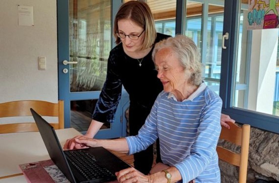 Helferin unterstützt Seniorin am PC.