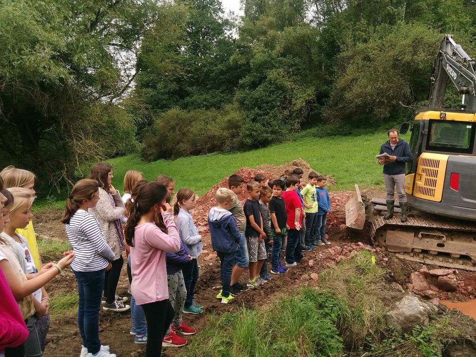 Alexander Hammel vom städtischen Tiefbauamt (r.) erläutert Kindern der Grundschule Irsch Details der Bauarbeiten zum Blauen Klassenzimmer und zur Renaturierung des Irscher Bachs. Foto: Tiefbauamt Trier