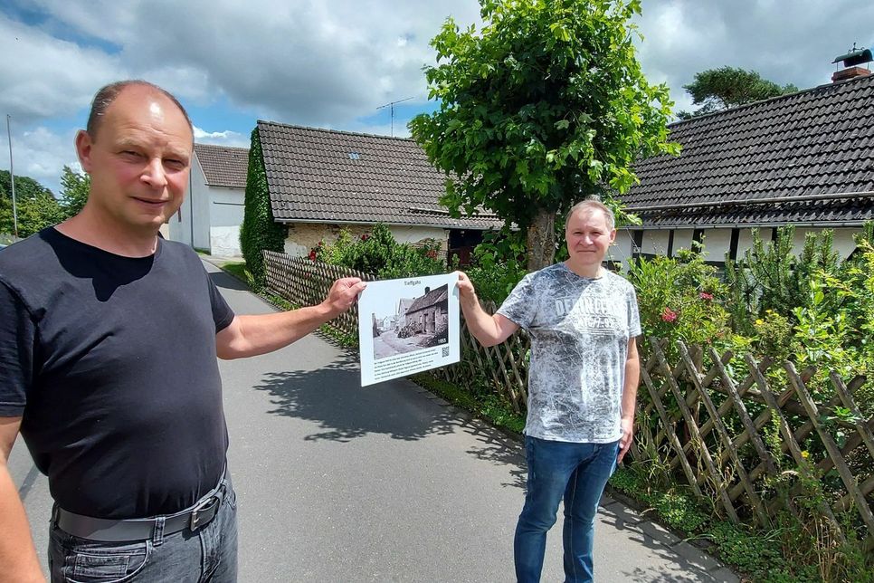 Rainer Reetz und Michael Pauels präsentieren eins von insgesamt 52 Schildern, welche die Namen und Geschichte alter Häuser und Straßen im Eifeldorf Mülheim dokumentieren.  mn-Fotos