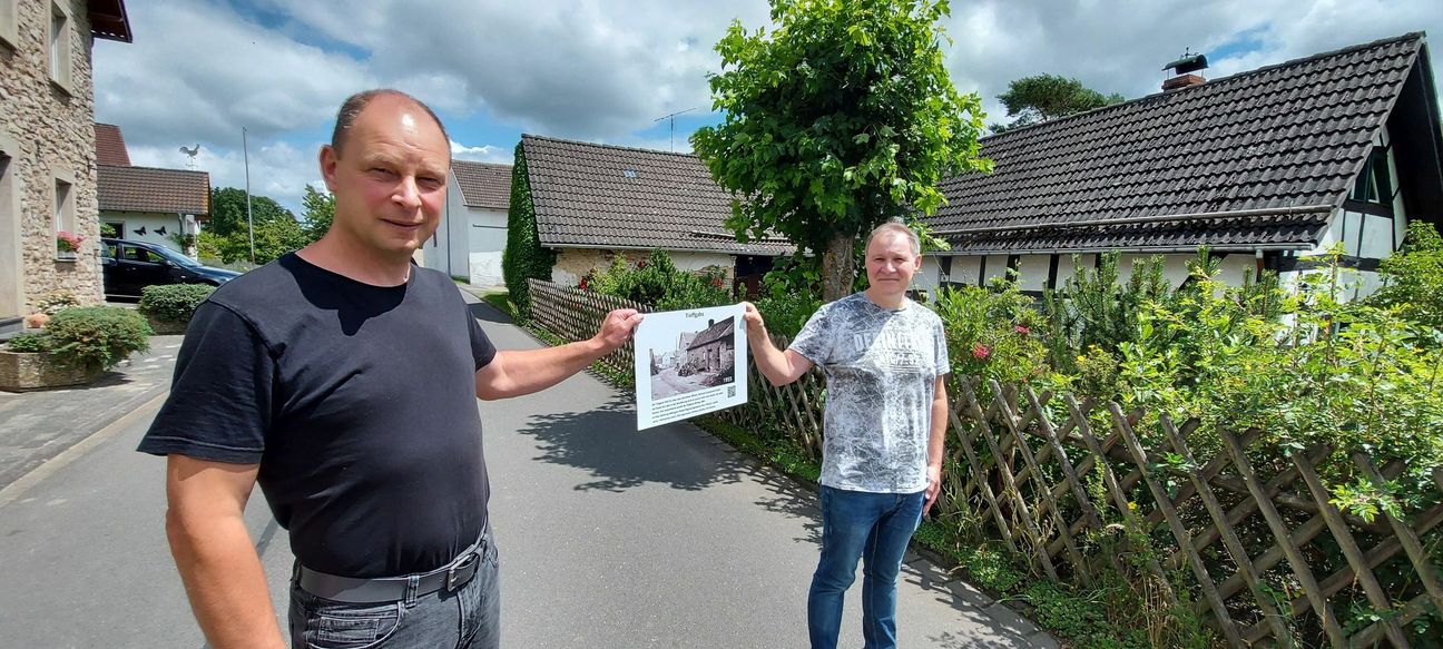 Rainer Reetz und Michael Pauels präsentieren eins von insgesamt 52 Schildern, welche die Namen und Geschichte alter Häuser und Straßen im Eifeldorf Mülheim dokumentieren.  mn-Fotos