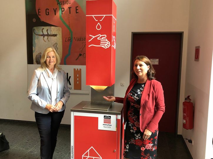 Dagmar Wirtz, geschäftsführende Gesellschafterin der »Machbarmacher«, präsentiert Margareta Ritter den innovativen Desinfektionsspender, der den Gästen der Monschauer Tourist-Info seit Wiedereröffnung mehr Schutz bietet. Foto: T. Förster