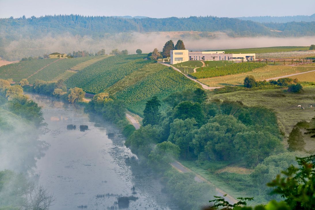 Die neue Manufaktur auf dem Wiltinger Schlossberg ist hoch über die Saar gelegen. Das Gebäudeensemble aus Produktions- und Präsentationsräumen folgt dem Vorbild einer preußischen Wein-Domäne. Der Monolith ist unterirdsich durch den Holzfasskeller mit der Produktion verbunden.