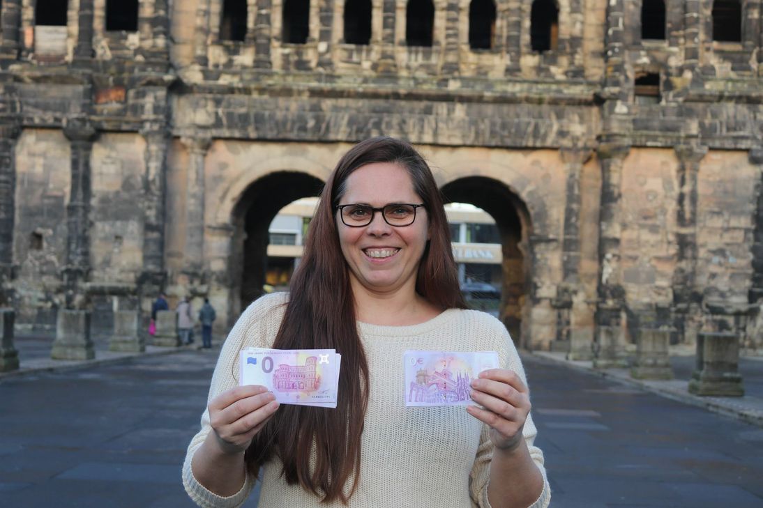 Caroline Baranowski, ttm-Abteilungsleiterin, mit der violetten Banknote vor der Porta Nigra. Foto: Trier Tourismus und Marketing GmbH.