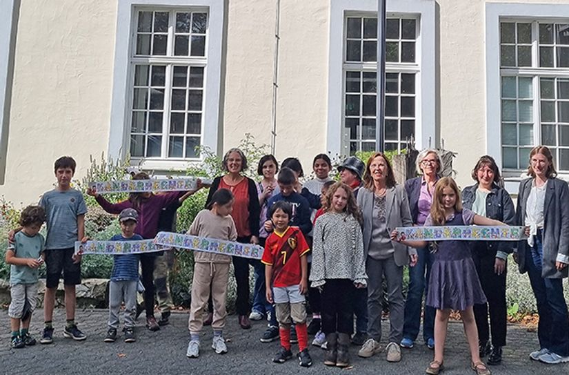 Auf Einladung des Trikis-Büros präsentieren Kinder aus Georgien, Pakistan und Ägypten, die derzeit in der Aufnahmeeinrichtung betreut werden, die gelbe Kinderrechte-Fahne vor dem Rathaus zusammen mit Bürgermeisterin Elvira Garbes