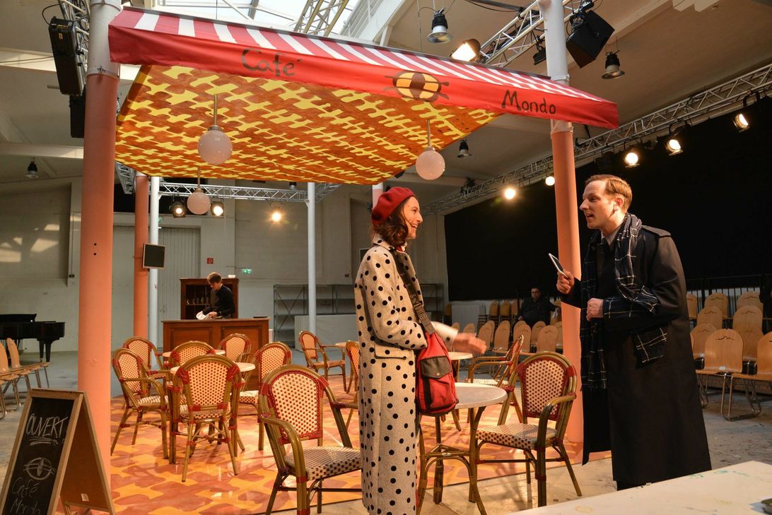 Die politisch links gerichtete Mado (Marsha Zimmermann) lernt den rechtsgerichteten Alexandre (Martin Geisen) in einem Café kennen. Von den politischen Präferenzen des Gegenübers ahnen sie jedoch zunächst nichts. Im Hintergrund ist Intendant Manfred Langner zu sehen, der das Stück "Politisch korrekt" inszeniert. Foto: Presseamt Trier