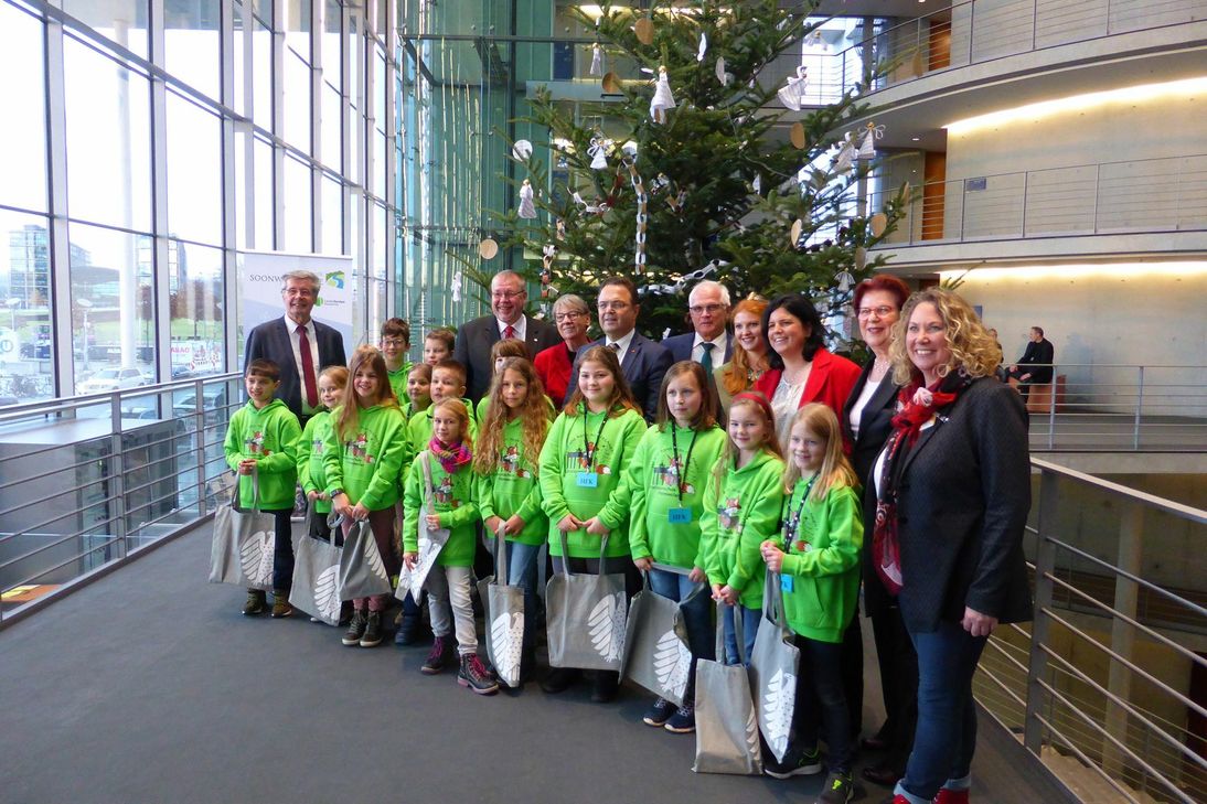 Zusammen mit Schülern der Lützelsoonschule Hennweiler (Vordergrund) übergibt Naturpark-Vorsitzende Bettina Dickes (1. v.r.) zusammen mit Präsident des Verbands Deutscher Naturparke, Friedel Heuwinkel (1. v.l.) und Soonwaldfee Lara Rennette (4. v.l.) den Weihnachtsbaum aus dem Naturpark Soonwald-Nahe an Bundestags Vizepräsidenten Dr. Hans-Peter Friedrich (4. v.l.) im Beisein der regionalen Bundestagsabgeordneten.