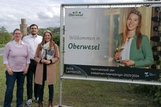 Zwei große Banner schmücken den Straßenrand: Mittelrhein-Weinkönigin Julia Lambrich (rechts) stellt gemeinsam mit Stadtbürgermeister Marius Stiehl (Mitte) und Franziska Schallop, Leitung der Tourist-Information (links) die neuen Banner vor.