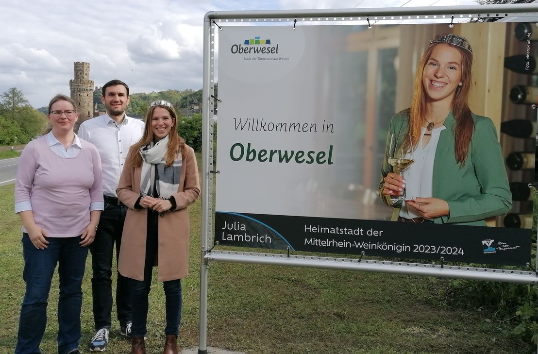 Zwei große Banner schmücken den Straßenrand: Mittelrhein-Weinkönigin Julia Lambrich (rechts) stellt gemeinsam mit Stadtbürgermeister Marius Stiehl (Mitte) und Franziska Schallop, Leitung der Tourist-Information (links) die neuen Banner vor.