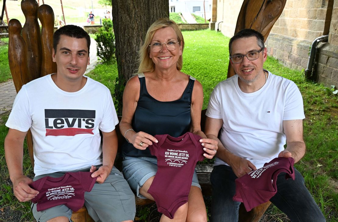 Die Beigeordnete Michaela Christmann-Bott präsentiert den Baby-Body gemeinsam mit Ortsbürgermeister Marcus Röth (links) und dem Beigeordneten Oliver Wilbert (rechts).