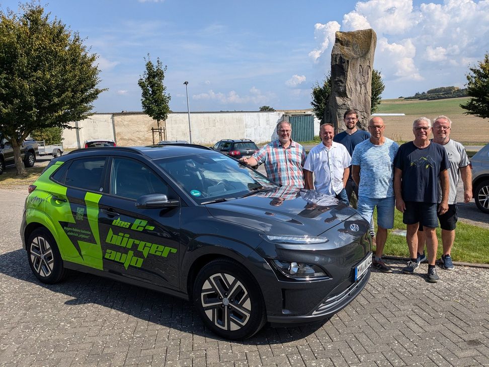 Ortsvorsteher Sven Weber (ganz links), Klimaschutzmanager Helge Lippert (3. von links) zusammen mit den vier Kümmerern präsentieren das Dorfauto am Bürgerhaus Hausen.