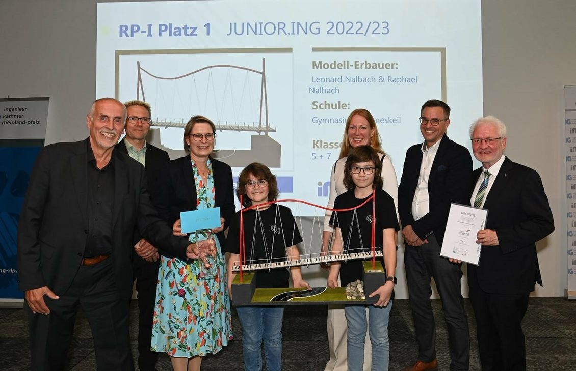 Dr. Gerhard Muth (Jury), Vorstandsmitglied der Ingenieurkammer, Volker Tschiedel (Jury), rheinland-pfälzisches Ministerium für Bildung, Bildungsministerin Dr. Stefanie Hubig, Dipl.-Ing. Katharina Häuser, Kammervorstandsmitglied, Prof. Dr.-Ing. Christian Glock von der RPTU (Jury) sowie Präsident Dr.-Ing. Horst Lenz (v.l.n.r. hintere Reihe) gratulieren den Siegern Raphael (vorne links) und Leonard Nalbach (vorne rechts) aus der 5. und 7. Klasse vom Gymnasium Hermeskeil ganz herzlich zum 1. Platz in der Altersgruppe I.