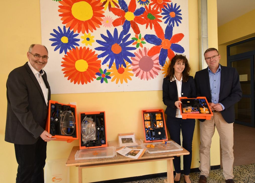 Markus Lüttger (rechts), Bürgermeister der Verbandsgemeinde Rüdesheim, und Friedrich Reinhardt (links), Innogy-Kommunalbetreuer, bei der Übergabe der Koffer an Schulleiterin Sandra Wolf (Mitte).