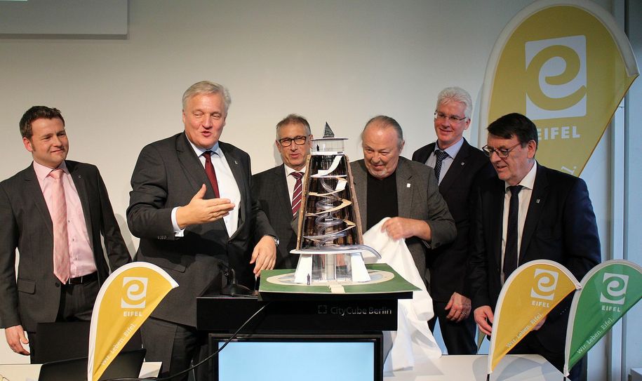 Der Künstler Rainer Arke (3.v.r.) enthüllte sein Modell des „Eifel.Turms“ der in Raffelsbrand errichtet werden soll. Marco Schmunkamp (v.l.), Landrat Wolfgang Spelthahn, Peter Cremer, Ingo Esser und Axel Buch schauten gespannt auf den fast 45 Meter hohen Holzkohlemeiler. Foto: Thomas Schmitz/pp/Agentur ProfiPress