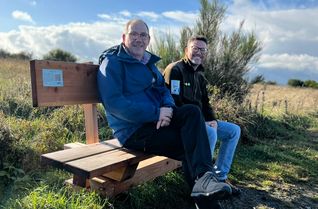 Edgar Dartenne (l.), dessen Urgroßvater die Hofstelle Gier errichtete, und Tobias Wiesen, Leiter Kommunikation beim Nationalpark Eifel, auf der Ruhebank, die mit einer kleinen Plakette Einblicke in das Schicksal der einstigen Bewohner der Dreiborner Hochfläche bietet.