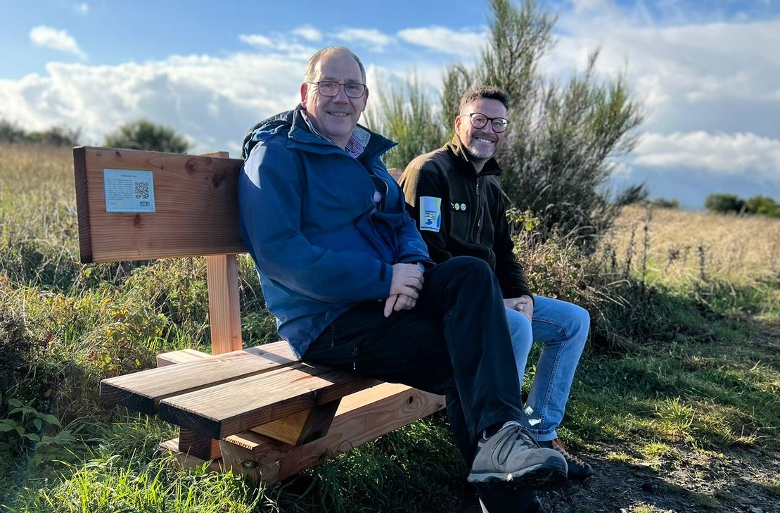 Edgar Dartenne (l.), dessen Urgroßvater die Hofstelle Gier errichtete, und Tobias Wiesen, Leiter Kommunikation beim Nationalpark Eifel, auf der Ruhebank, die mit einer kleinen Plakette Einblicke in das Schicksal der einstigen Bewohner der Dreiborner Hochfläche bietet.