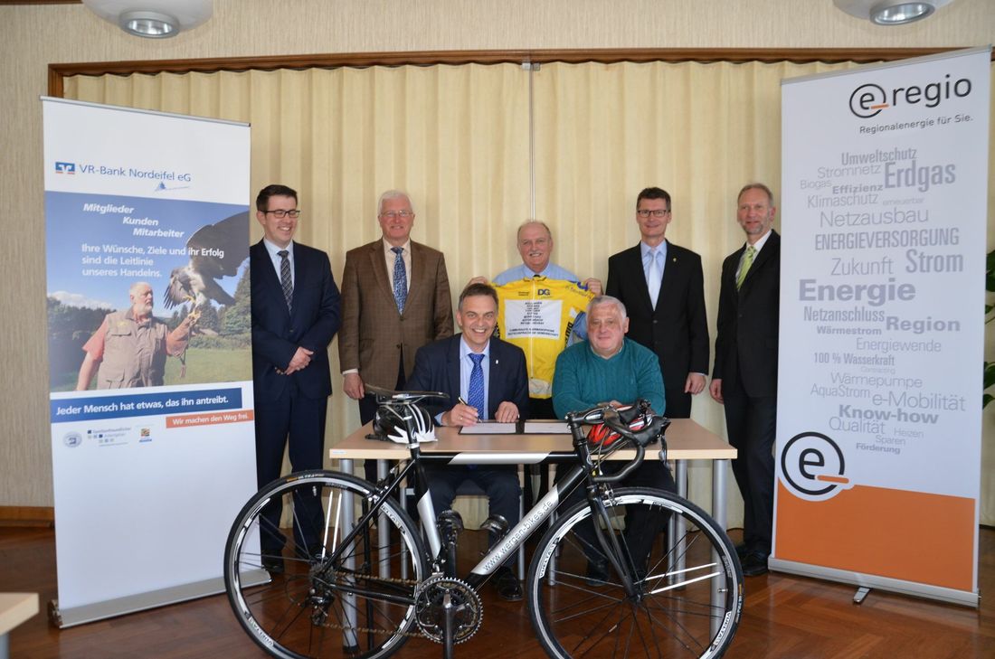 Bürgermeister Rudolf Westerburg und Rennleiter Christian Lebeau (vorne) unterzeichnen den Drei-Jahres-Vertrag für die Teilnahme der Gemeinde Hellenthal am Radklassiker »Triptyque Ardennais«.