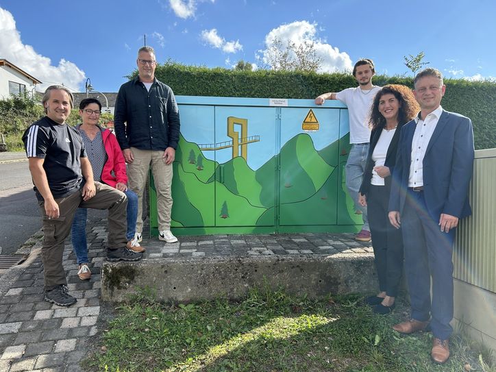 Begutachten gemeinsam das neue Kunstwerk auf der Trafostation in Hilscheid (v. l.): Zweiter Beigeordneter Rouven Bruce Schording, Gemeinderatsmitglied Karla Haink-Schmidt, Ortsbürgermeister Heiko Ennulat, Künstler David Rausch, Bürgermeisterin Vera Höfner sowie Westenergie-Regionalmanager Marco Felten.