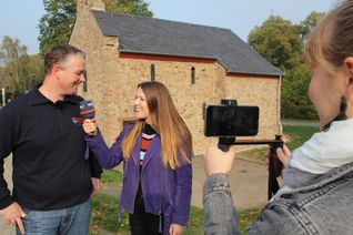 Wachendorfs stellvertretender Löschgruppenführer Marco Kaudel wird vor der Petruskapelle von WDR-Moderatorin Sandra Jozipovic interviewt. Lena Bauer filmt die beiden. Foto: Thomas Schmitz/pp/Agentur ProfiPress