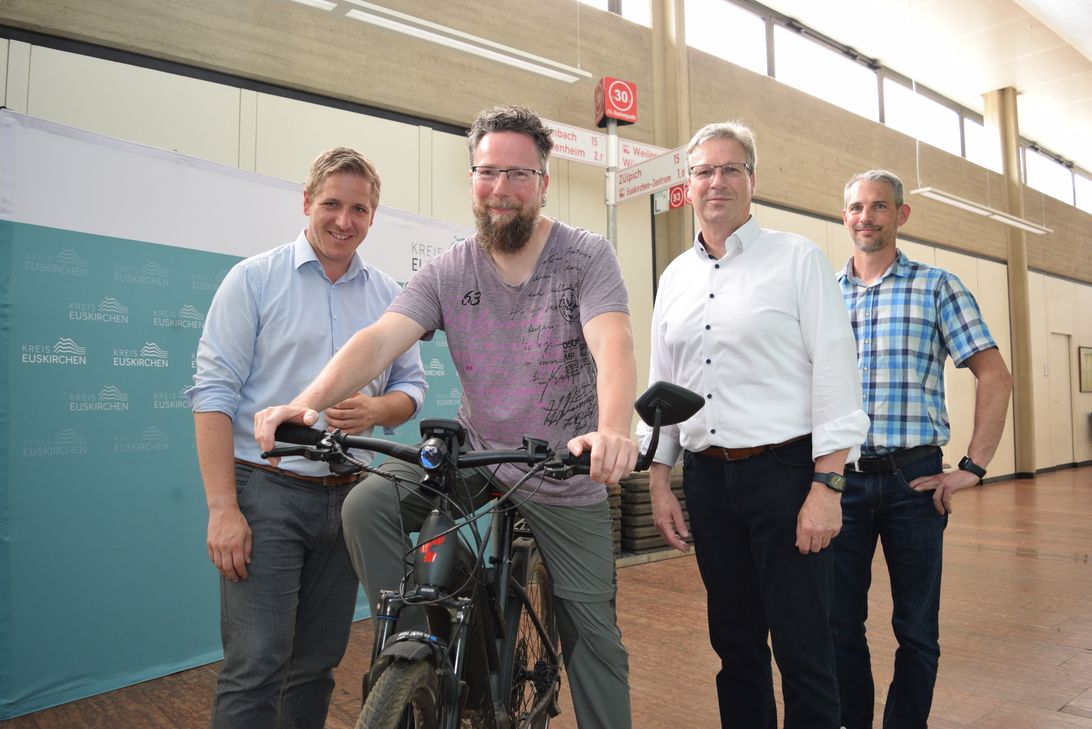 Radeln im Kreishaus? Nur bei diesem Foto. Ursprünglich war der Pressetermin mit Landrat Markus Ramers (v.li.), dem Fahrradbeauftragten des Kreises Markus Sprung, Achim Blindert, Allgemeiner Vertreter des Landrats und Guido Schmitz, Kreis-Bauhof, zur Vorstellung des Knotenpunktsystems in Elsig und Open-Air geplant. Aufgrund einer Unwetterwarnung war man jedoch nach drinnen ausgewichen. Im Hintergrund ist dennoch ein Beispiel für einen Knotenpunkt zu sehen.