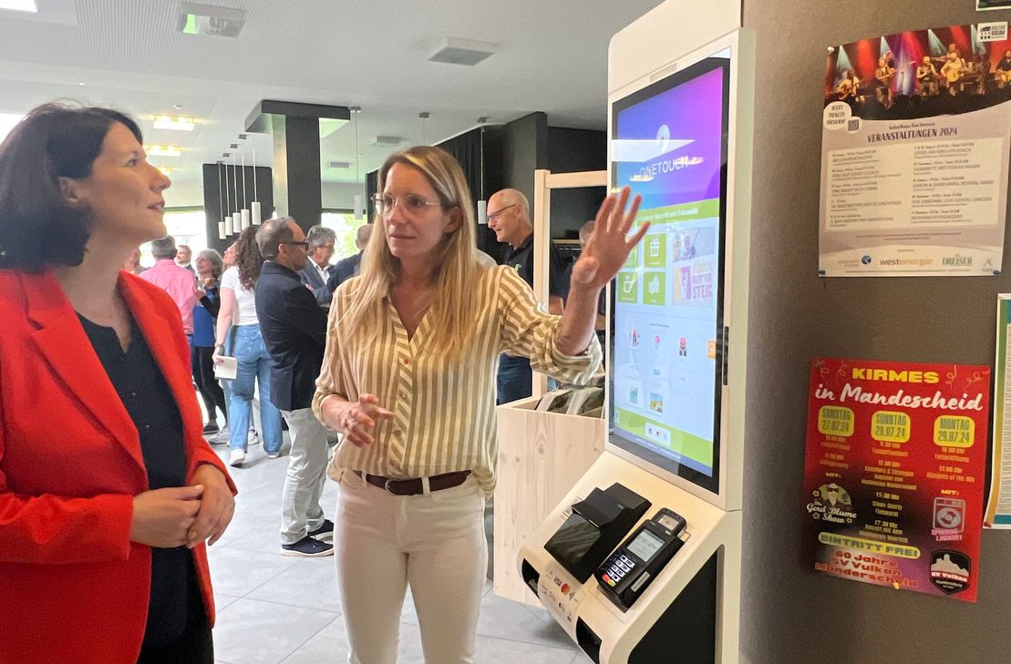 Vera Esch zeigt Staatsministerin Daniela Schmitt das neue Selbstbedienungsterminal, dass den Verleihprozesses der Klettersteigausrüstung vereinfacht und weitere Services bietet