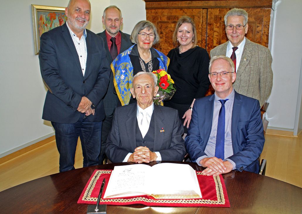 Im Vordergrund: Alfred Girault vor dem Gästebuch der Stadt Trier mit Oberbürgermeister Wolfgang Leibe. Hintere Reihe: Der Ortsvorsteher von Feyen-Weismark Rainhart Lehnart; Rüdiger Bisdorf, 1. Vorsitzender der TG Trier 1880;  Ehefrau Irene Girault; Tochter Cécile Girault; Matthias Kapp, Abteilungsleiter Leichtathletik und Trainer.  Foto: Stadt Trier, Presseamt