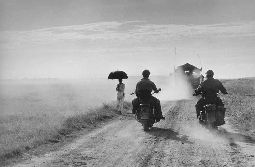 Capa Motorcyclists and woman walking on the road from Nam Dinh to Thai Binh Indochina (Vietnam) May 1954 (c) Robert Capa (c) International Center of Photography Magnum Photos