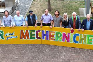 Viel Lust auf ein großes, fröhliches Stadtfest macht das knallbunte, vom Mechernicher Kurator Franz Kruse (5. v.re.) entworfene Kunstwerk, das die Musiker und Verantwortlichen nun vor dem Rathaus präsentierten.