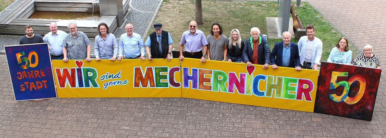 Viel Lust auf ein großes, fröhliches Stadtfest macht das knallbunte, vom Mechernicher Kurator Franz Kruse (5. v.re.) entworfene Kunstwerk, das die Musiker und Verantwortlichen nun vor dem Rathaus präsentierten.