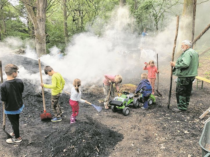 Der Nationalpark Eifel feiert seinen »Europäischen Tag der Parke« am Sonntag, 12. Juni, inmitten der 7. Düttlinger Meilertage. Der erfahrene Köhlermeister Gerd Linden (re.) führt auch bereits die Düttlinger Jugend an die alte Tradition heran - wie hier beim »Kindermeiler« 2019.
