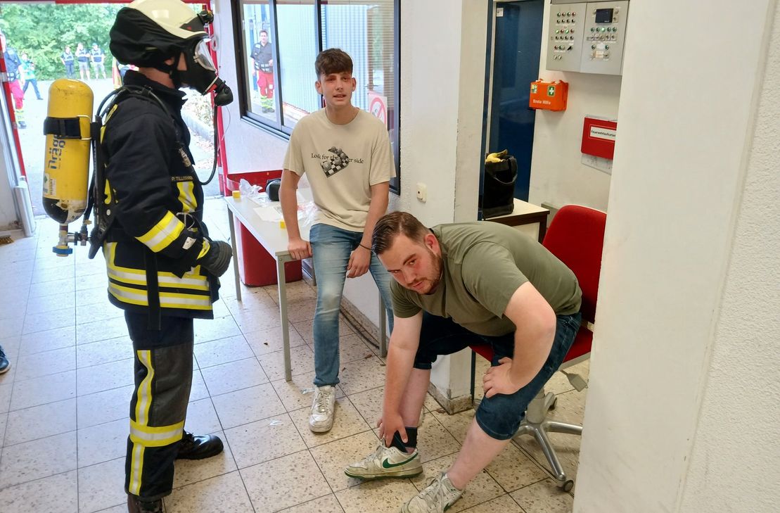 Vor Schmerzen krümmen: zwei "verletzte" Mitarbeiter des Supermarkts werden von einem Feuerwehrmann in Atemschutz betreut.