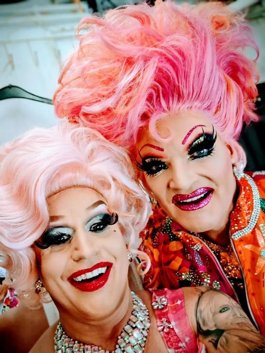 Travestiekünstlerin Regina Red (links) und Olivia Jones lachen gemeinsam in die Kamera. Beide tragen bunte Perücken, auffälliges, farbenfrohes Make-up und posieren fröhlich für ein Selfie.
