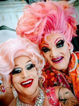 Travestiekünstlerin Regina Red (links) und Olivia Jones lachen gemeinsam in die Kamera. Beide tragen bunte Perücken, auffälliges, farbenfrohes Make-up und posieren fröhlich für ein Selfie.