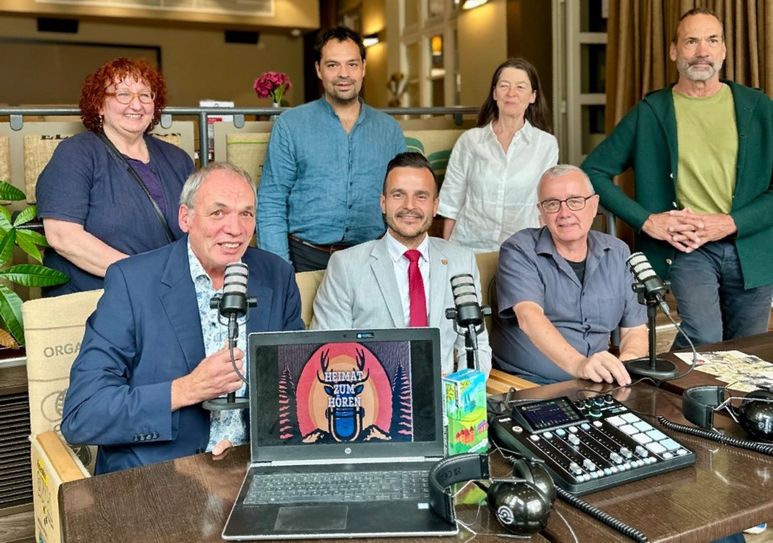 Der Vorstand der Edgar Reitz Filmstiftung (v.l.: Christine Schleindl, Mathias Reitz Zausinger, Susanne Reitz und Christian Reitz) bietet beim Ortstermin eine Projekt-Kooperation an. Das Produktionsteam vom Podcast "Heimat zum Hören" (sitzend v.l.) freut sich über das Angebot: Thomas Vatheuer, Arianit Besiri und Alfons Schramer.